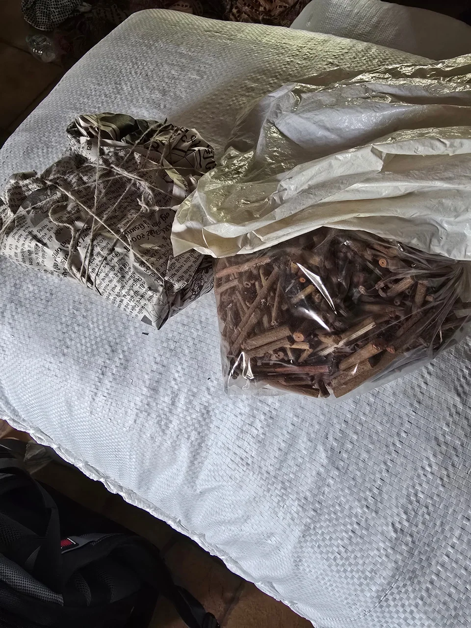 A bag of cut roots and stems for dyeing beside a newspaper parcel tied with jute twine