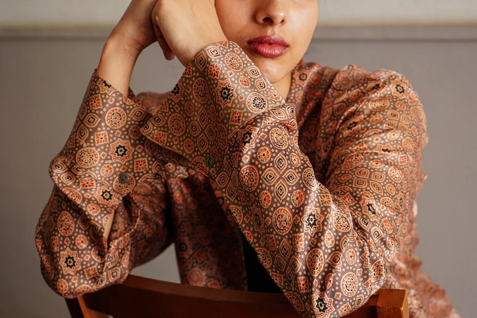 An ajrakh silk shirt in rust and mauve, worn with arms folded over the back of a wooden chair