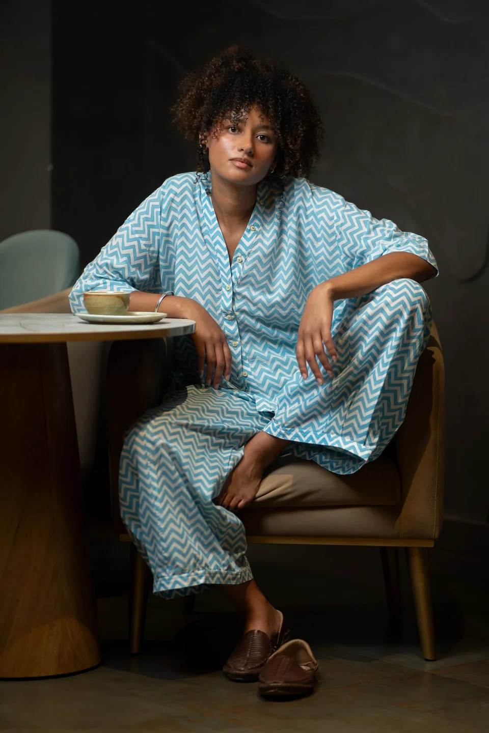 Block-printed blue shirt and trousers, seated at a small round table