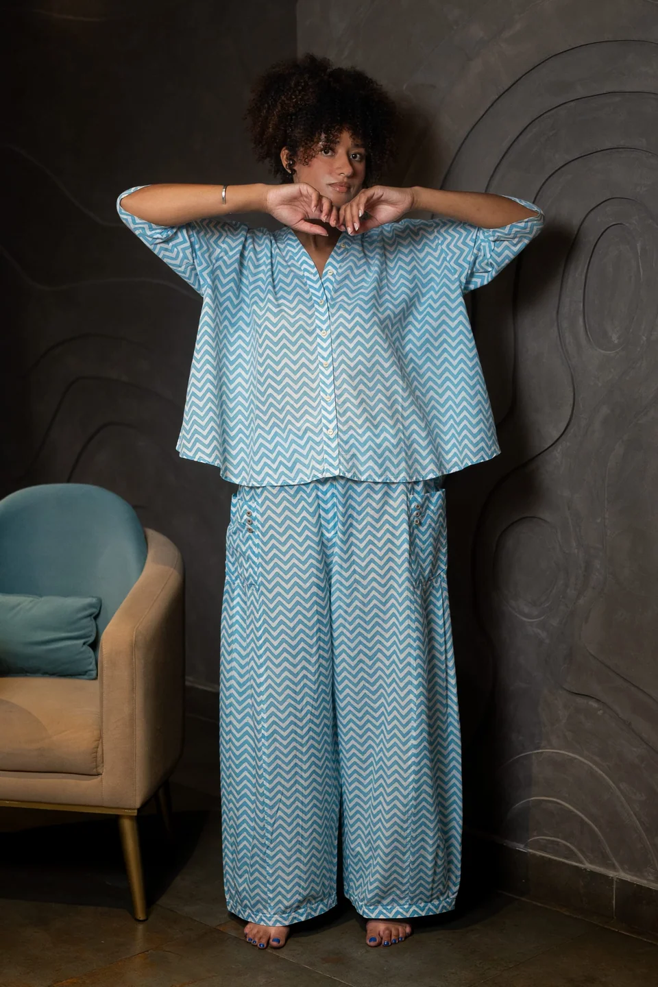 Blue chevron block-printed top and trousers worn together, arms folded overhead