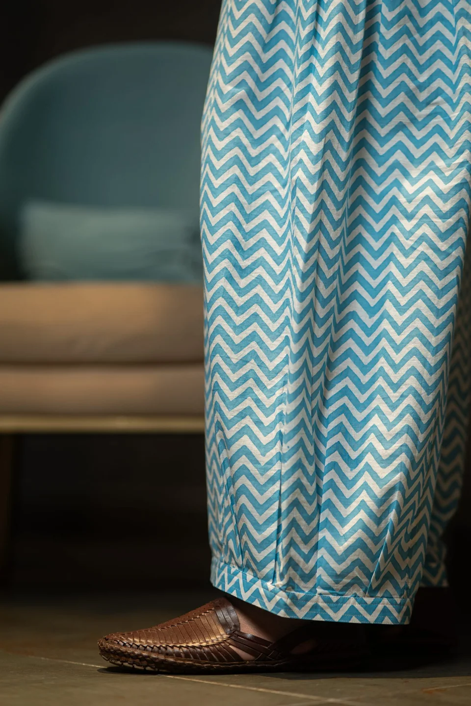 The hem of the blue chevron trousers over woven leather sandals