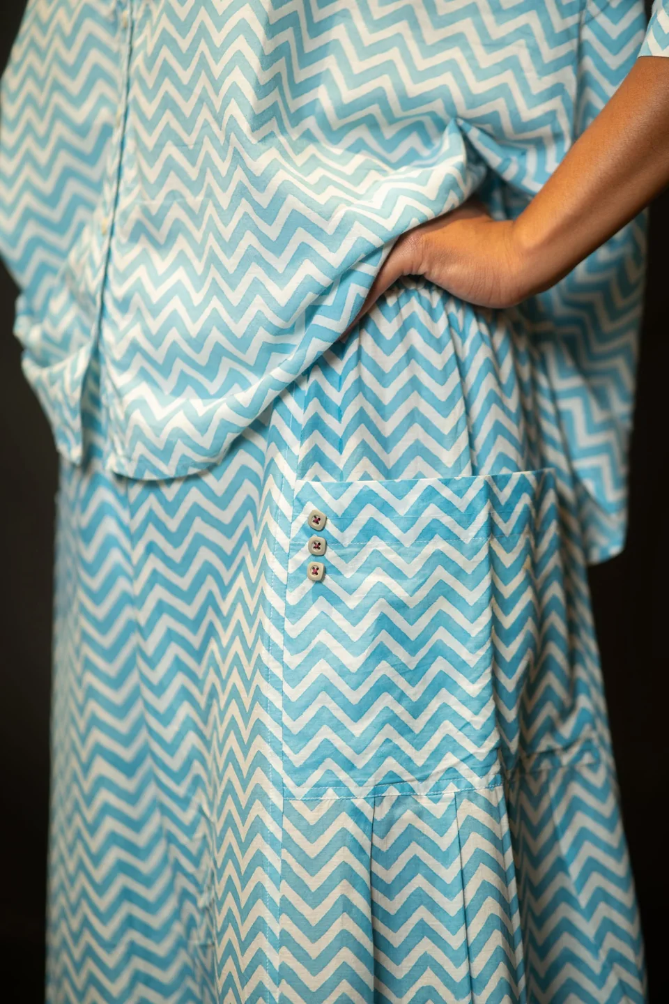 Hand resting at the hip pocket of the blue chevron trousers
