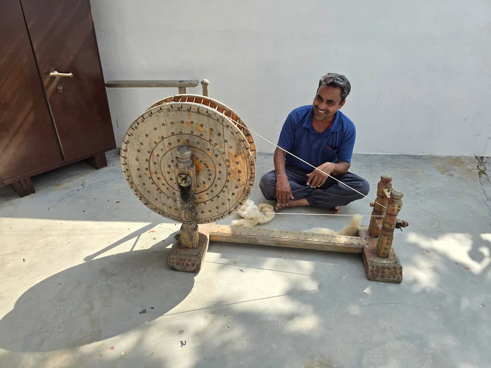 An artisan sitting on the floor spinning yarn on a charkha