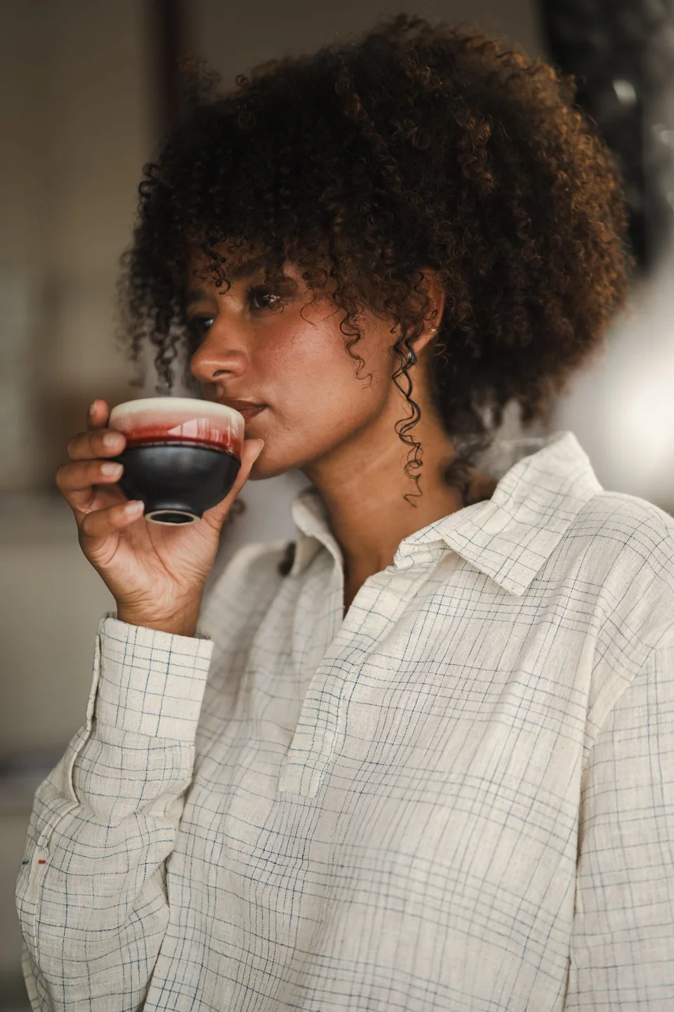 Handwoven checked shirt, holding a small cup of coffee