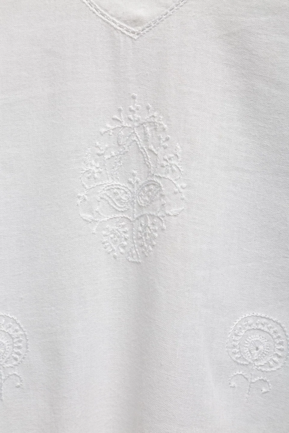 White chikankari motifs on a white cotton tunic, seen close below the neckline