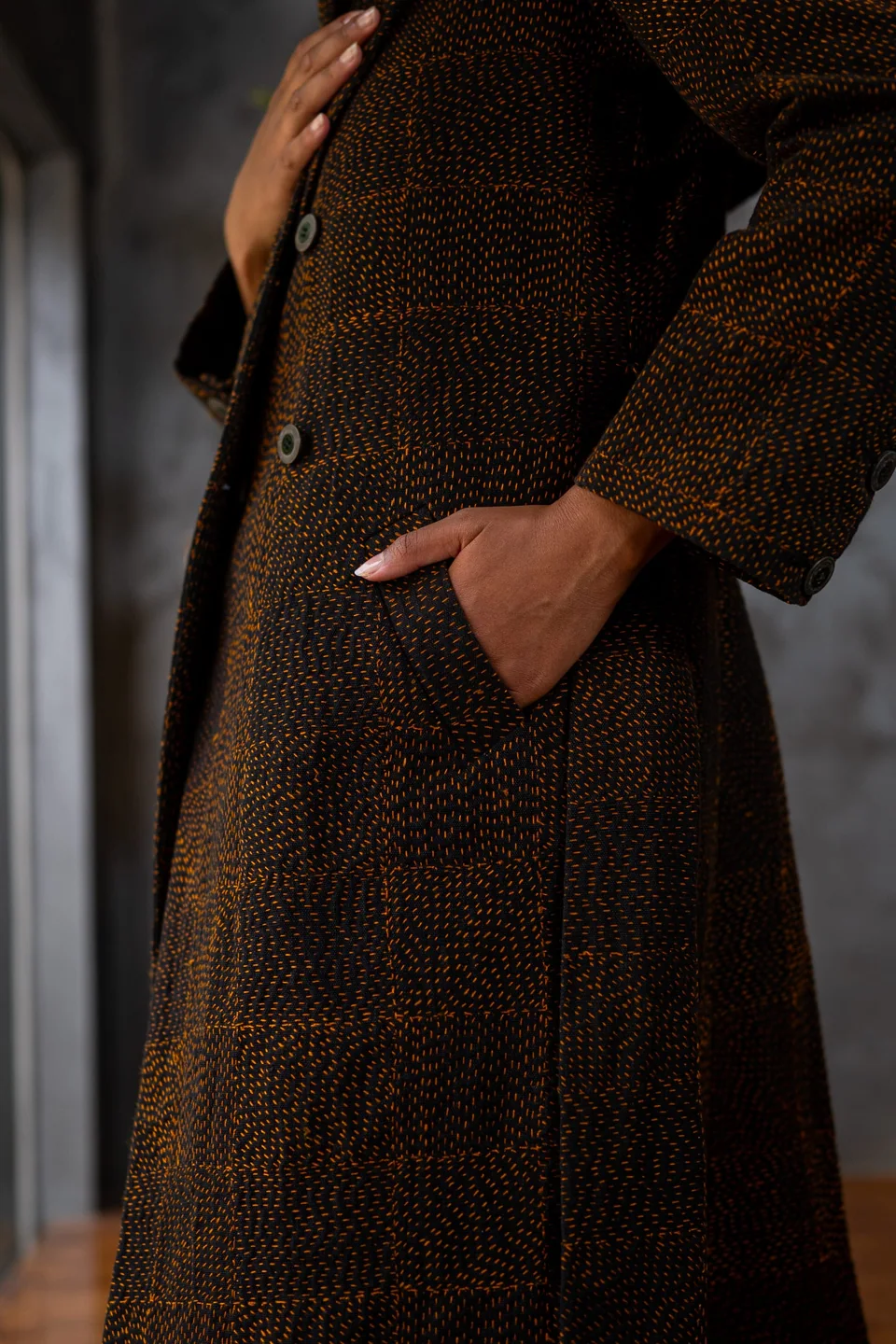 Long dark kantha coat worn with both hands in the pockets