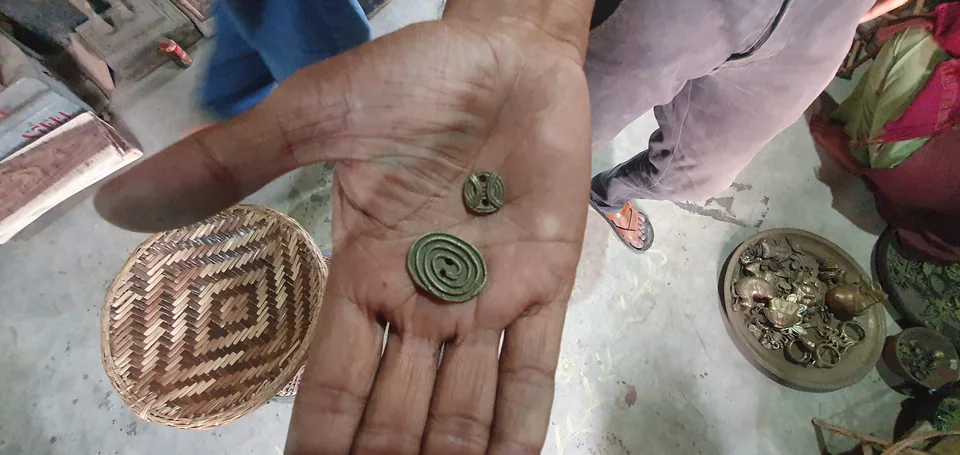An open palm holding two small dokra pieces in a village workshop