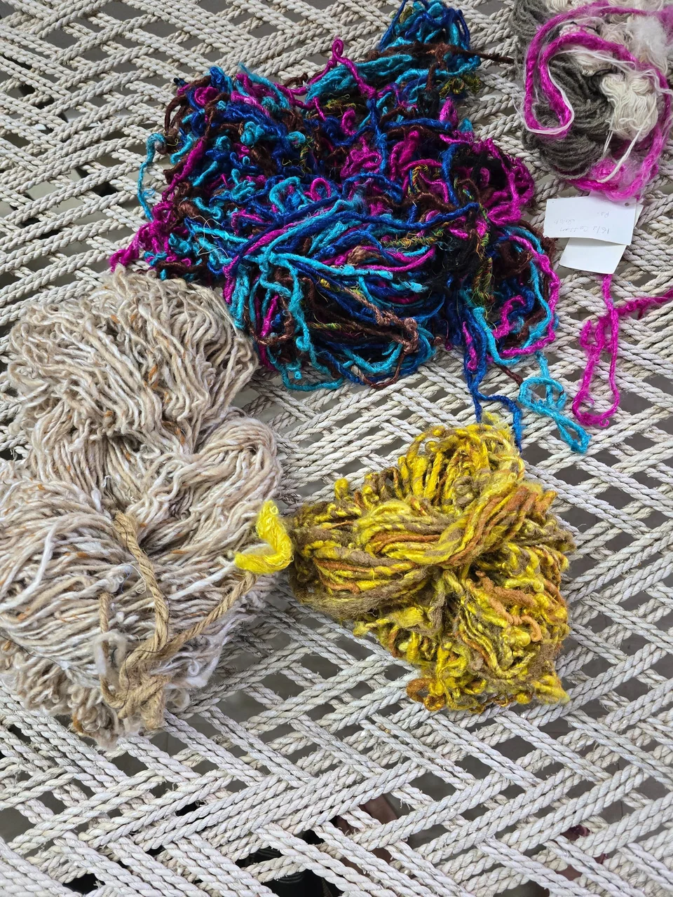 Skeins of dyed yarn in pink, blue and yellow on a woven cot