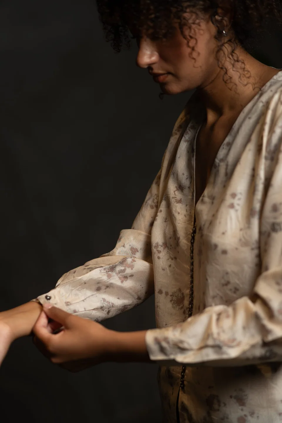 Hands adjusting the buttoned cuff of the eco-printed silk blouse