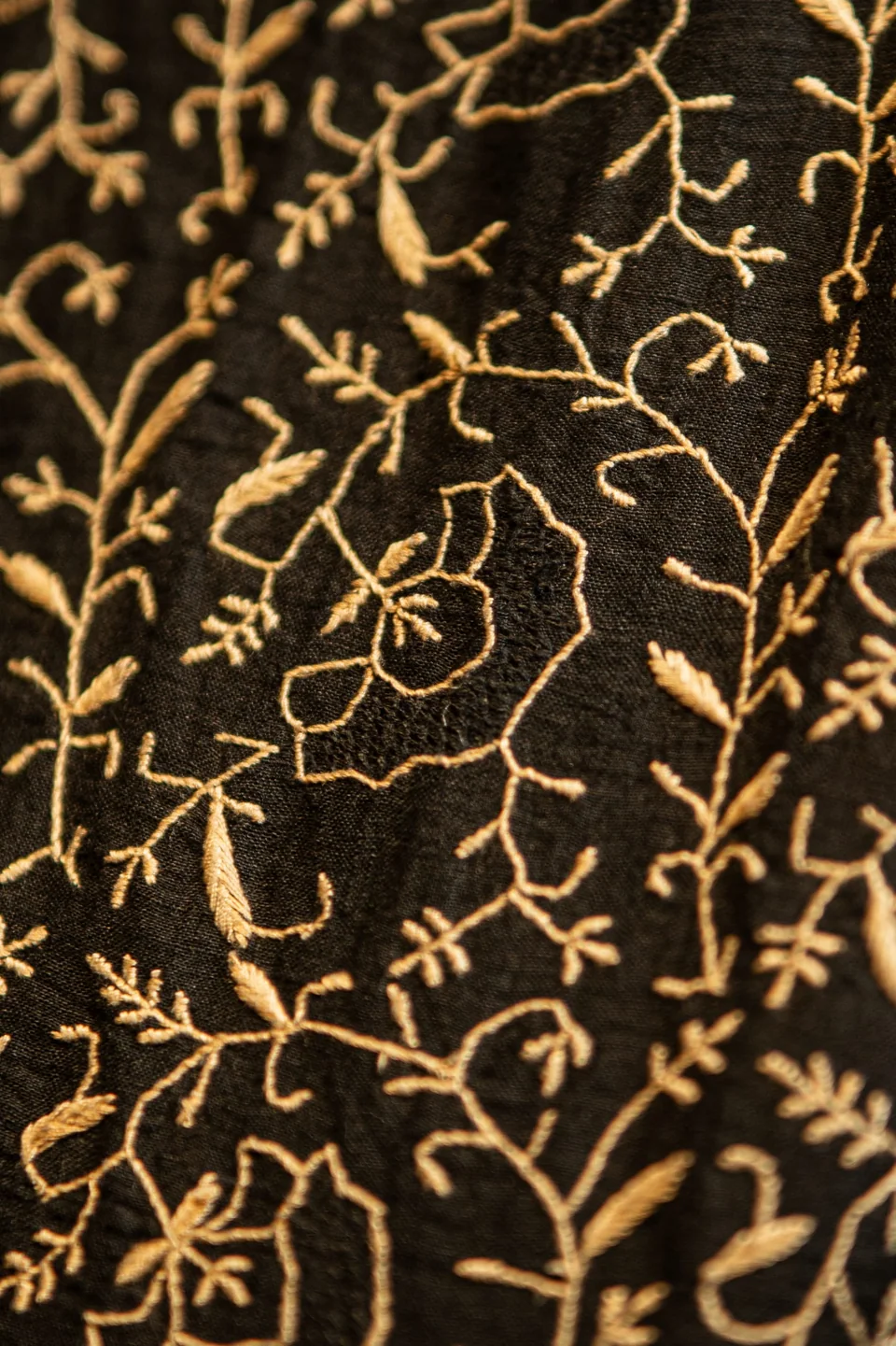 Close view of gold embroidered vines running across black cloth