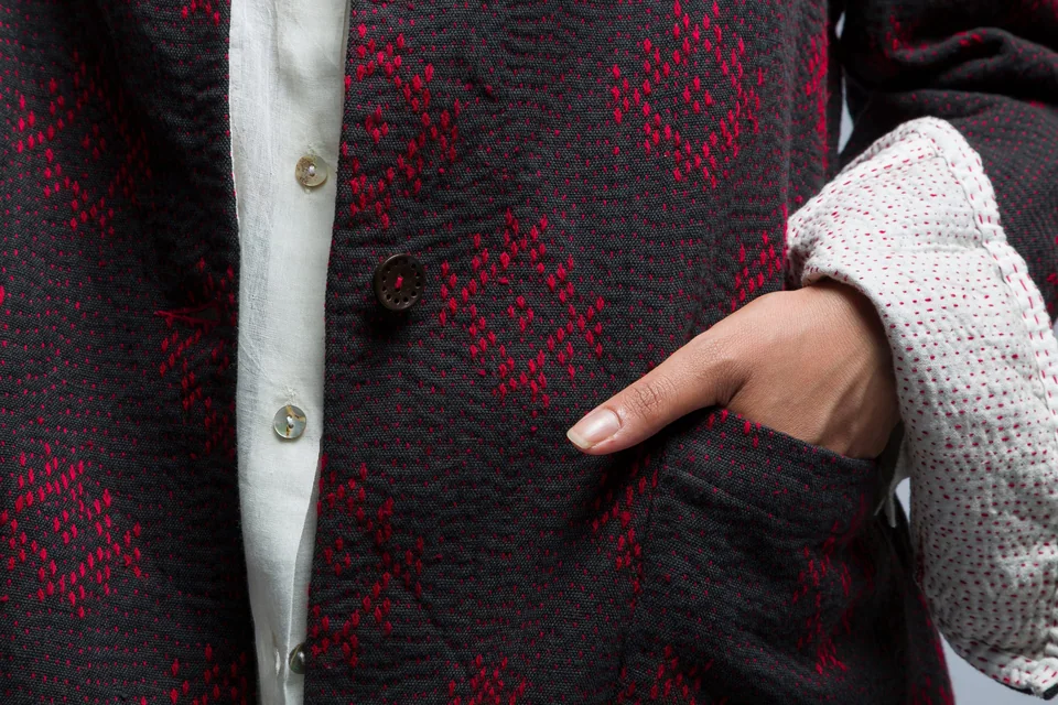 Pocket of a dark jacket with pink diamond embroidery, hand resting in it