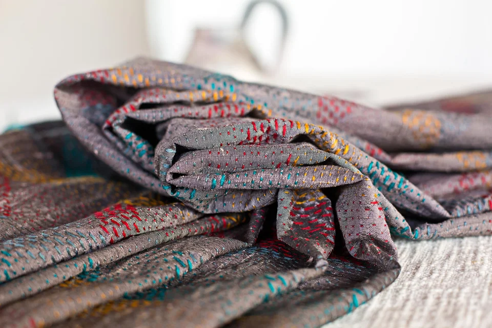A folded kantha coat, coloured running stitch travelling across grey