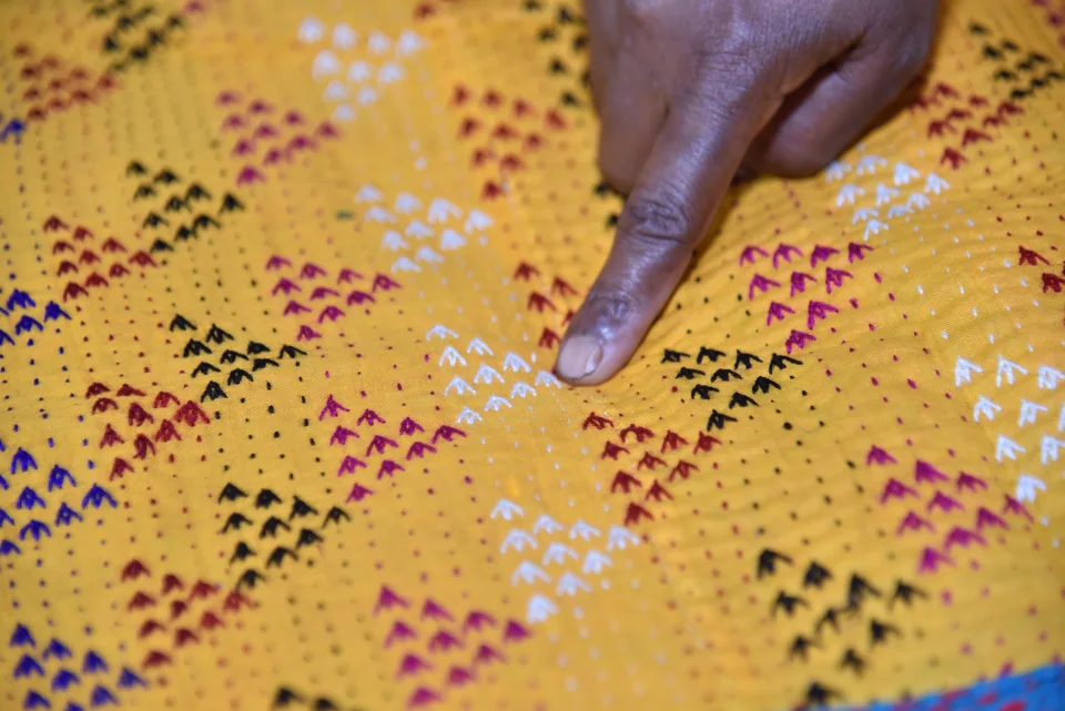 A hand resting on yellow cloth covered in small kantha triangles