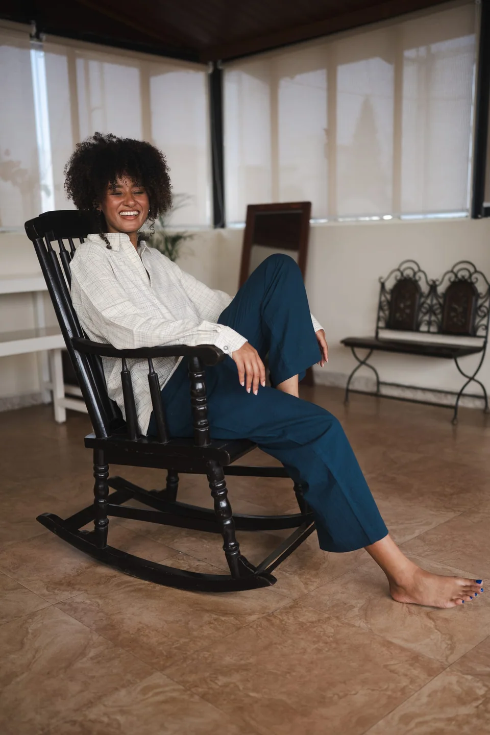 Seated barefoot in a rocking chair by a window, cotton shirt and indigo trousers