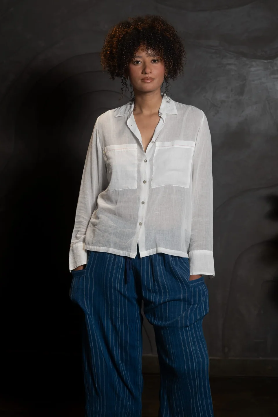 The sheer muslin shirt worn loose, hands in the trouser pockets