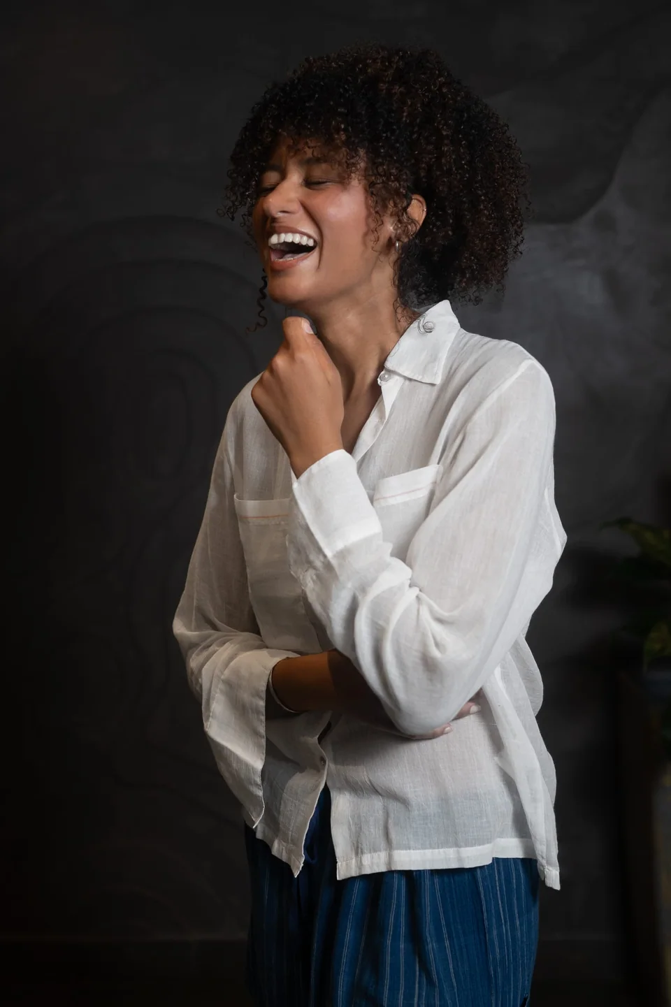 Laughing in the sheer muslin shirt, one hand at the collar