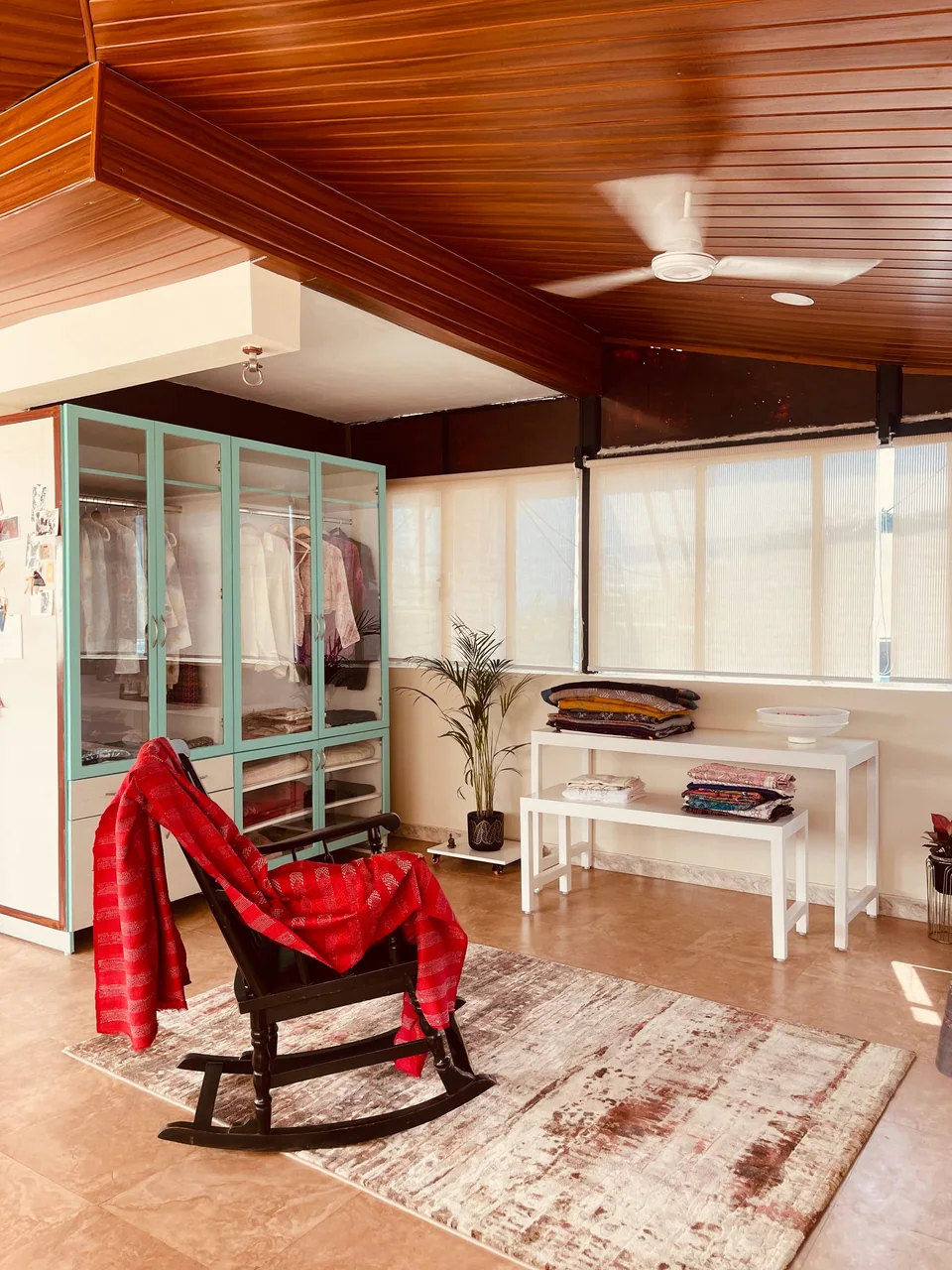 The studio with a red shawl draped over a rocking chair, glass wardrobes and a wooden ceiling