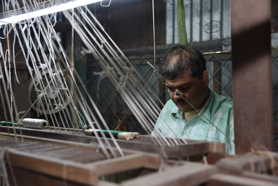 A weaver at his loom, drawing the warp threads through