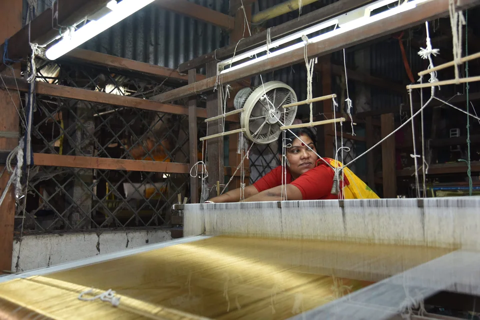 A weaver at a home loom, yellow silk warp catching the light