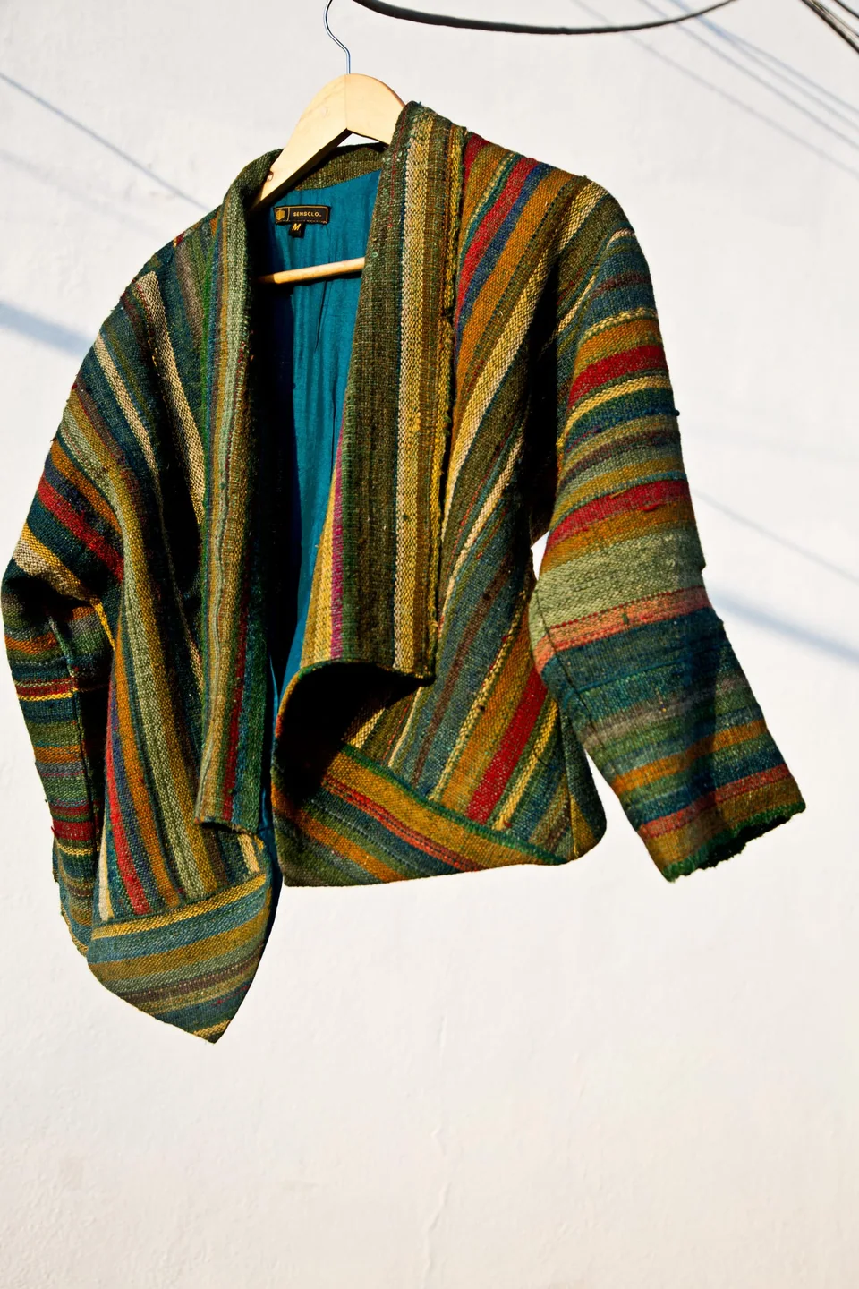 Handwoven wool jacket in green and gold stripes, hanging